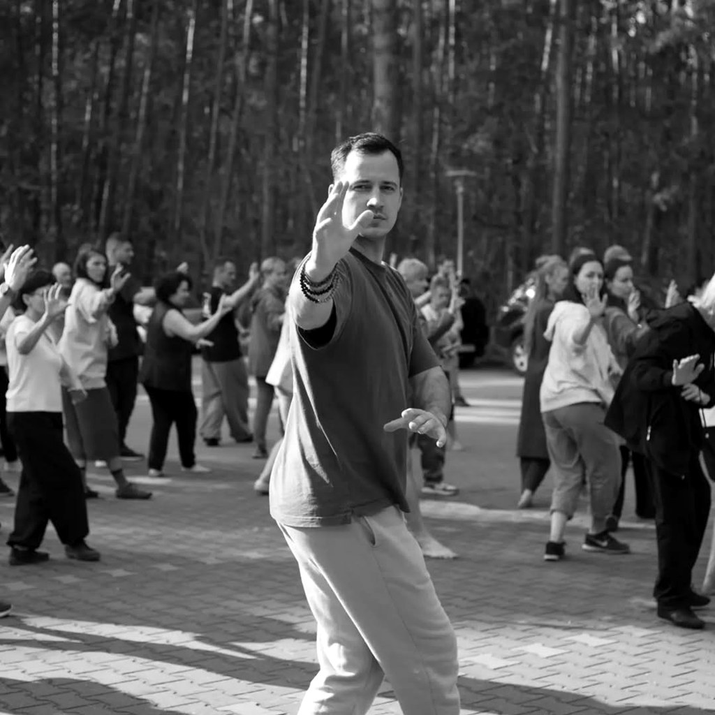 Karol Głogowski prowadzący zajęcia Qi Gong na zewnątrz, w tle grupa uczestników